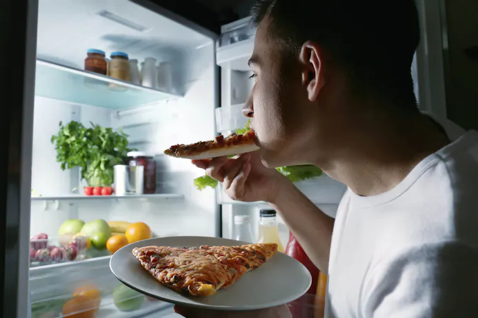 Man die midden in de nacht pizza eet uit de koelkast