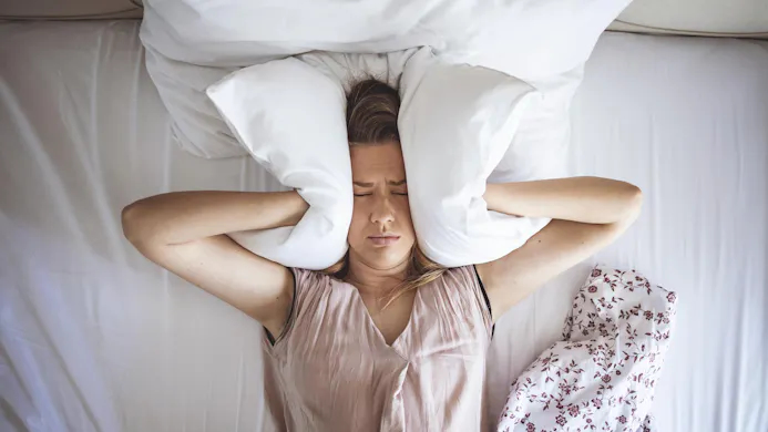 Vrouw in bed met kussen over haar oren wegens geluidsoverlast