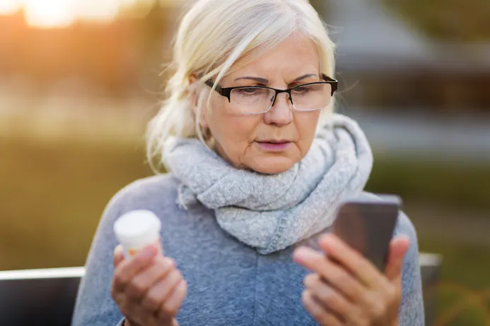 Vrouw met potje medicijnen in de ene hand en een smartphone in de andere hand