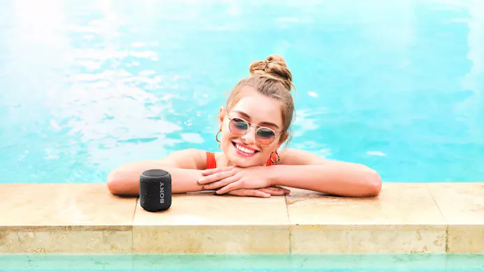 Sony-speaker en zwemster aan de rand van een zwembad.