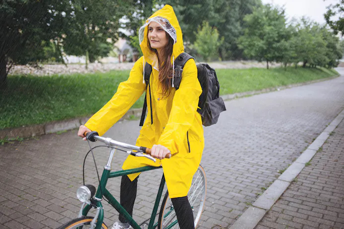 Vrouw op fiets in regen in gele regenjas