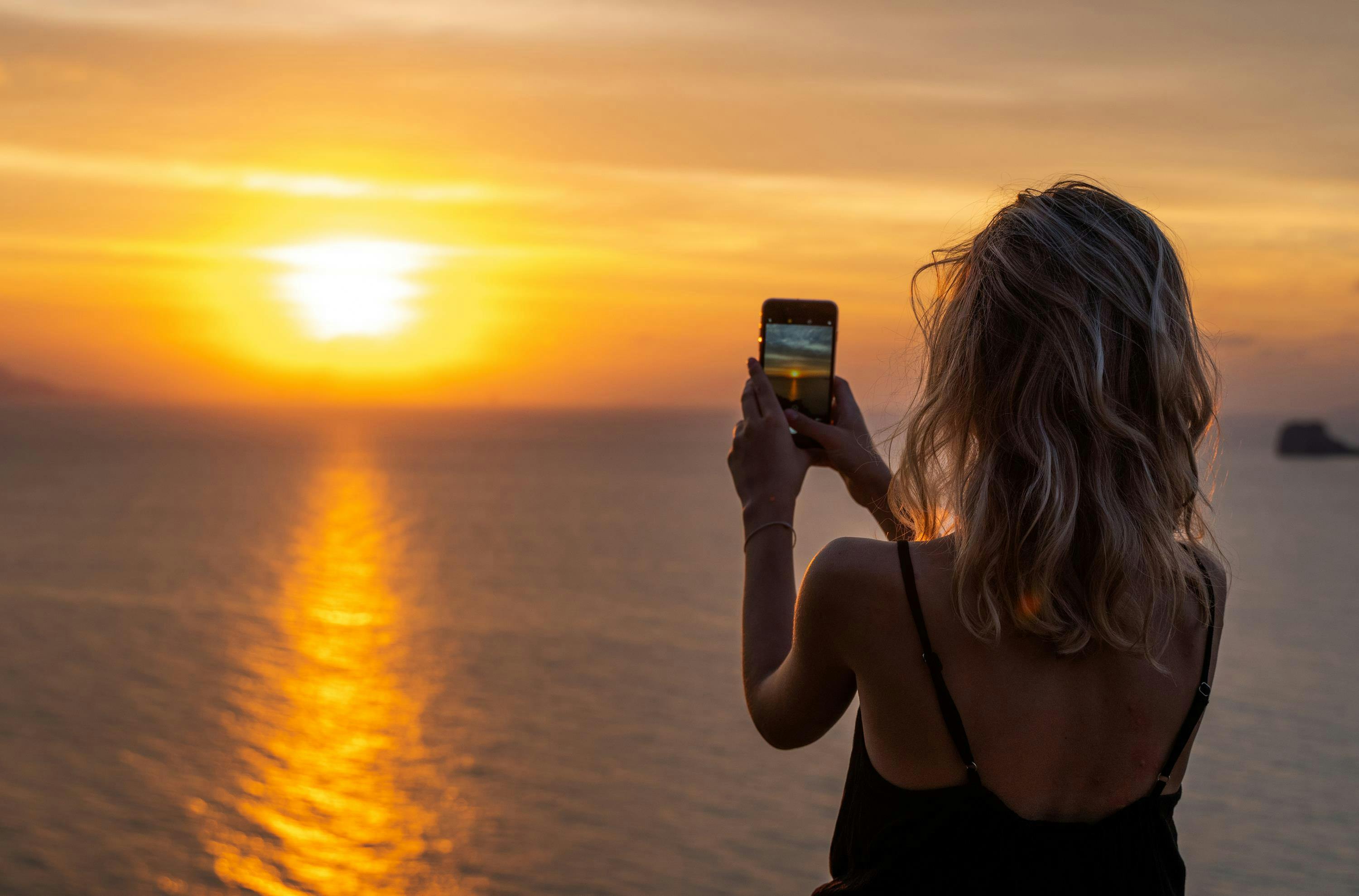 vrouw fotografeert de zonsondergang met een smartphone
